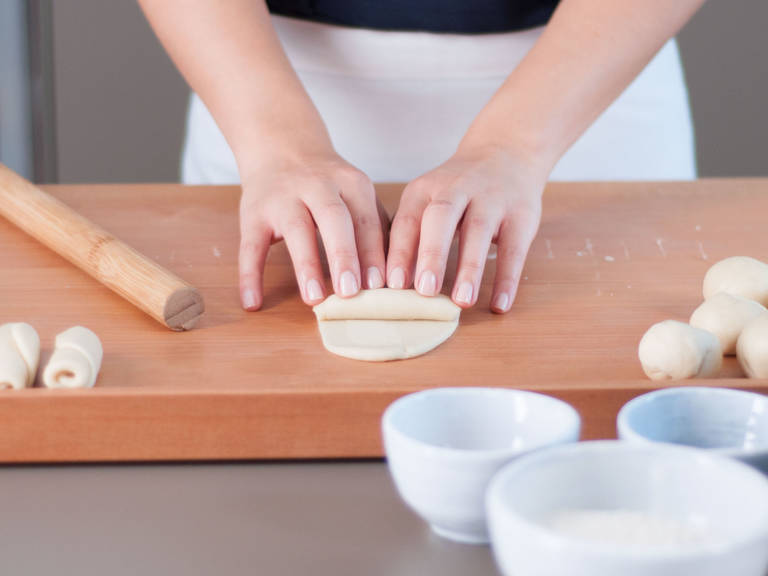 用擀面杖将包好的面团擀成椭圆形面饼，然后用手从下至上卷起面饼。